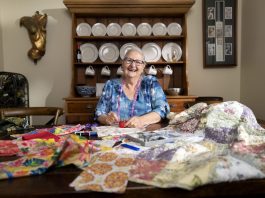 A woman sits happily at her table with several pieces of haberdashery in front of her